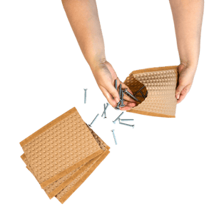 Hände füllen Schrauben in einen PapairBag, die gepolsterten Beutel aus PapairWrap, der Luftpolsterfolie aus Papier.