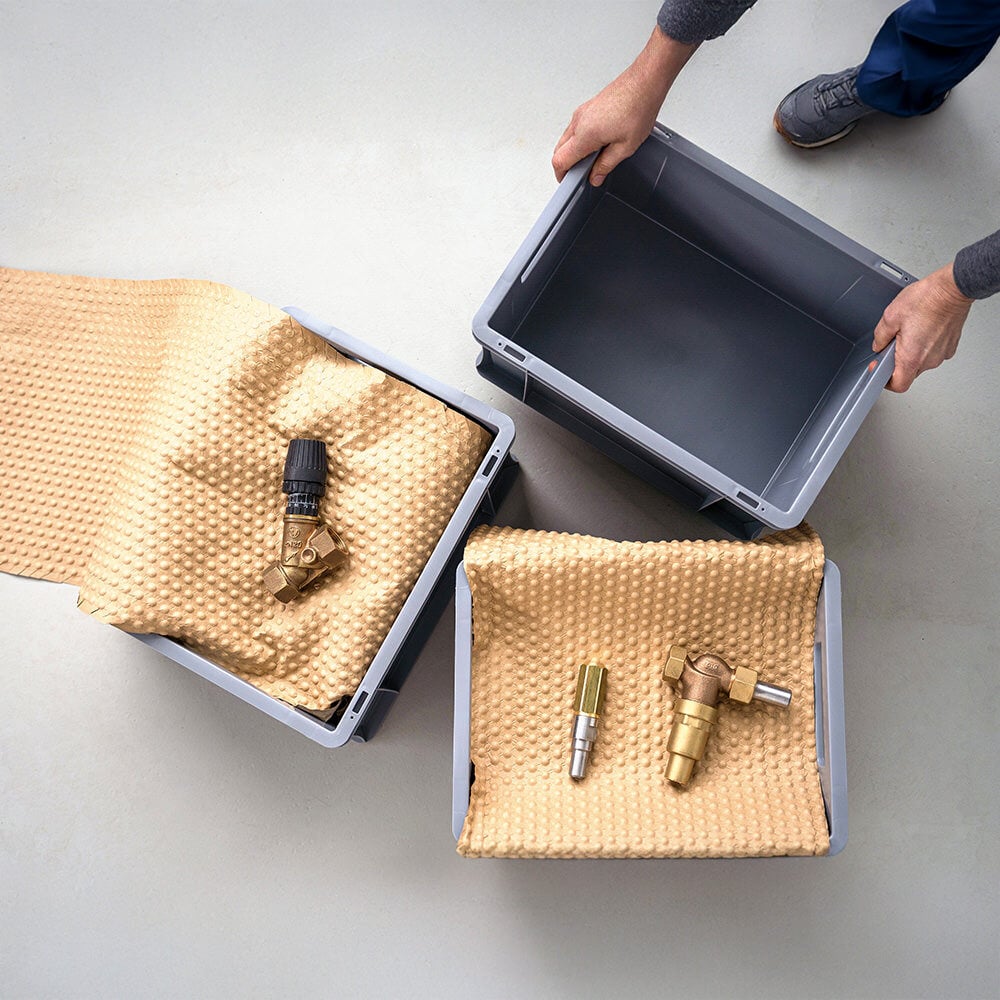 A production worker places a small load carrier next to two others with technical items padded in PapairWrap.